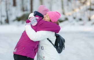 Kaksi naista halaa toisiaan talvimaisemassa.