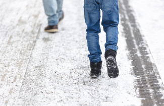 Kahden kulkijan jalat talvisella jalkakäytävällä.