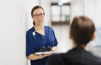 Sairaanhoitaja kannettavan tietokoneen kanssa katsoo asiakasta.