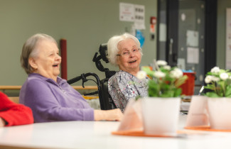 Kaksi ikääntynyttä naista nauravat pöydän ääressä.