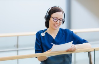 Sairaanhoitaja kirjoittaa lomakkeelle kuulokkeet päässä.