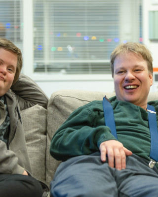 Kaksi miestä istuvat sohvalla hymyillen.
