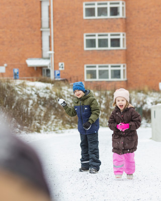 Kaksi lasta ulkoilemassa pihalla talvella.