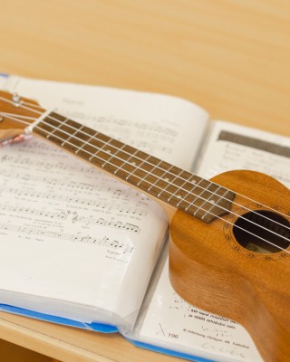 Kuvassa on ruskeanvärinen ukulele avoimen nuottikansion päällä.