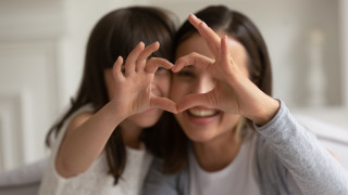Aikuinen nainen ja pieni tyttö muodostavat sormillaan sydämen.