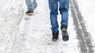 Kahden kulkijan jalat talvisella jalkakäytävällä.
