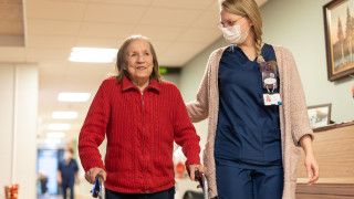 Ikääntynyt nainen ja hoitaja kävelevät käytävällä