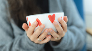 Lämmin sydänkuvioinen kahvikuppi ihmisen käsissä.