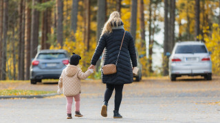 Äiti ja lapsi kävelemässä käsi kädessä parkkipaikalla.